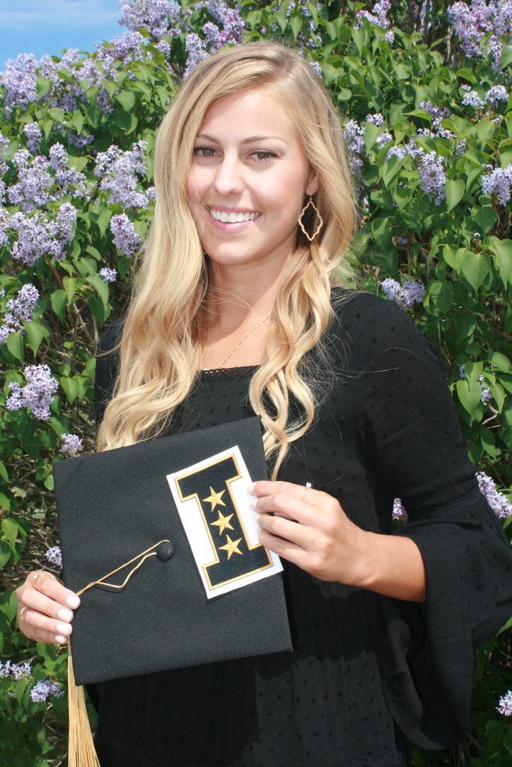 Woman with blond hair poses in graduation regalia