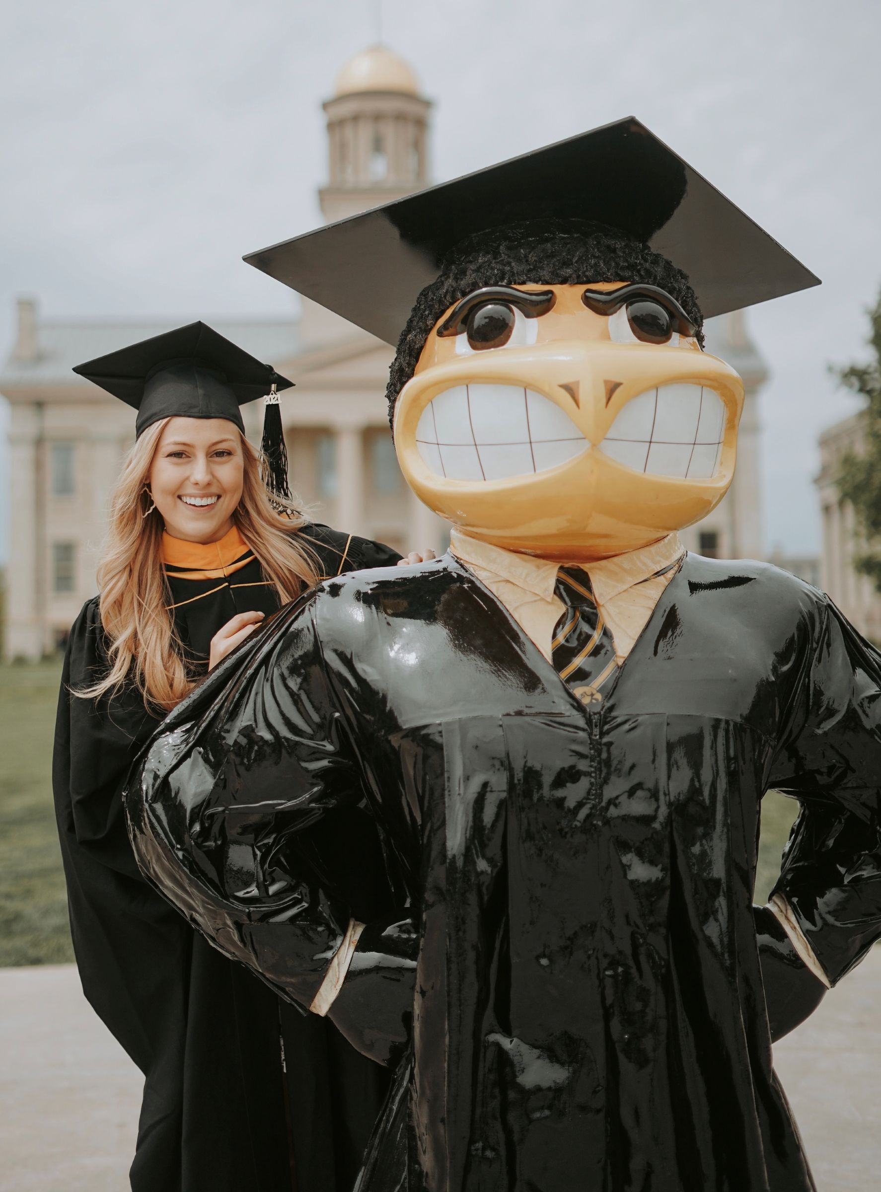 Woman in graduation gown poses with statue of Iowa mascot Herky