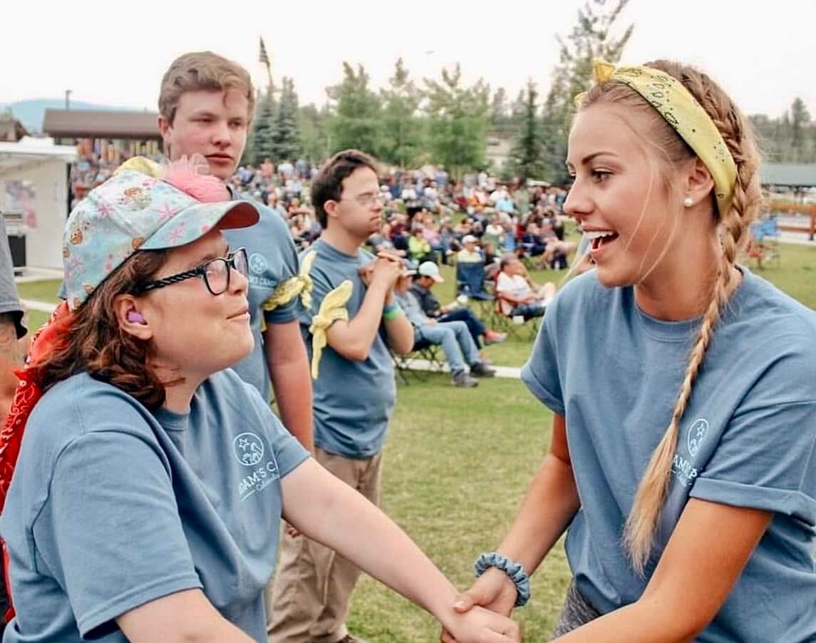 Two people wearing matching event T-shirts hold hands while talking at an outdoor community gathering.