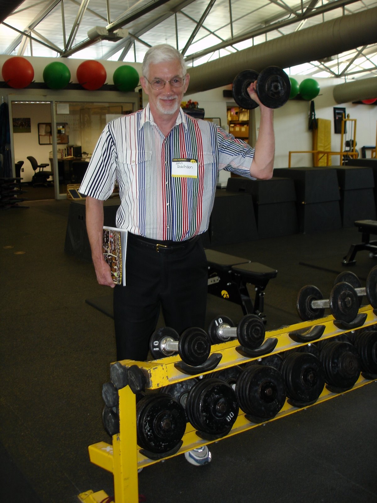 Person stands in a fitness center holding a dumbbell beside a rack of weights.