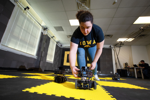 Camilla Tabasso, Undergraduate Student, bends over facing the camera to pick up a small robot car