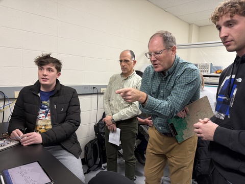 Man in blue-green shirt points while three others look on