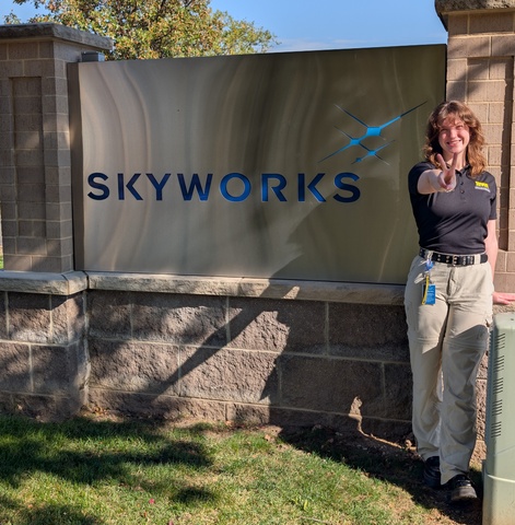 Woman with brown hair stands in front of Skyworks sign