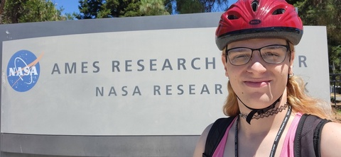 Person with bike helmet stands in front of NASA sign