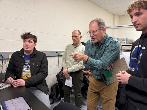 Man in blue-green shirt points while three others look on