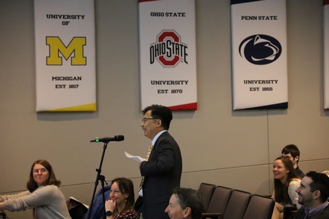 Man speaks surrounded by seated audience