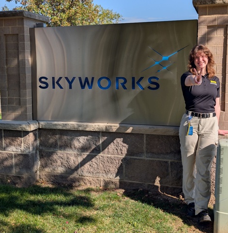 Woman with brown hair stands in front of Skyworks sign