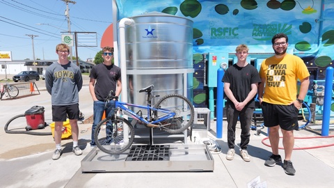 Four men pose with with silver water tank