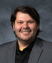 PhD student joe gomes smiling in a grey suit