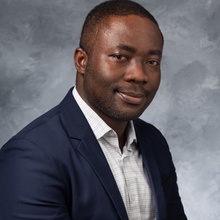 Head and shoulders portrait of man with short hair, dark suit coat, and white button down collared shirt