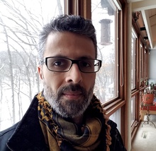 Professor with glasses and scarf poses in front of window