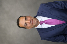 Karim poses for portrait wearing blue suit and purple tie