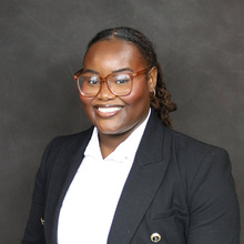 Portrait studio image of woman with dark hair and glass with dark suit coat and white shirt