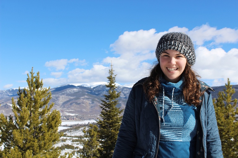 camryn in a knit hat standing in front of a mountain