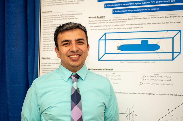 man in green shirt and purple tie smiling in front of research poster