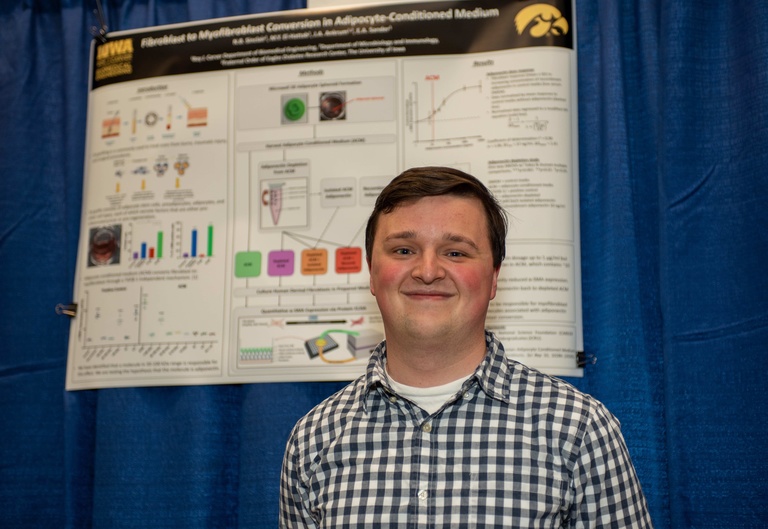 male student posing in front of his research poster