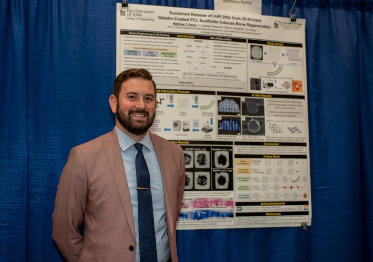 male student wearing a suit jacket and tie smiling in front of his research poster