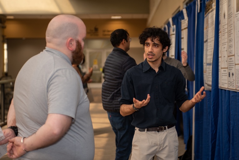 male student presenting his research poster to an onlooker