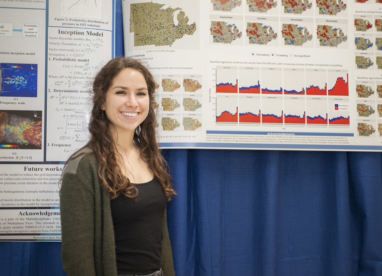 student smiling in front of research poster