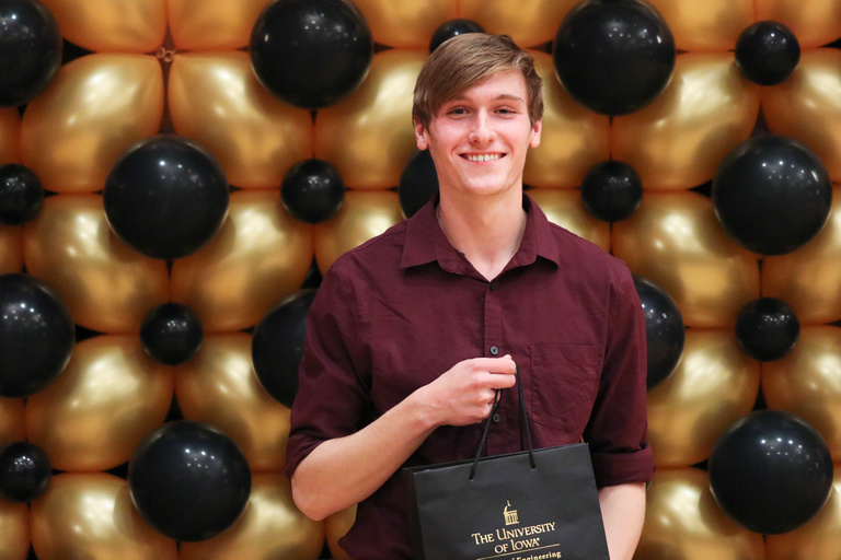 student holds bag in front of balloon wall 
