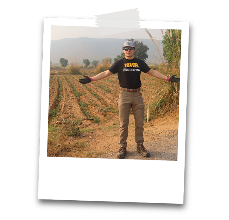 male student with Iowa Engineering shirt stands in front of a field with red dirt