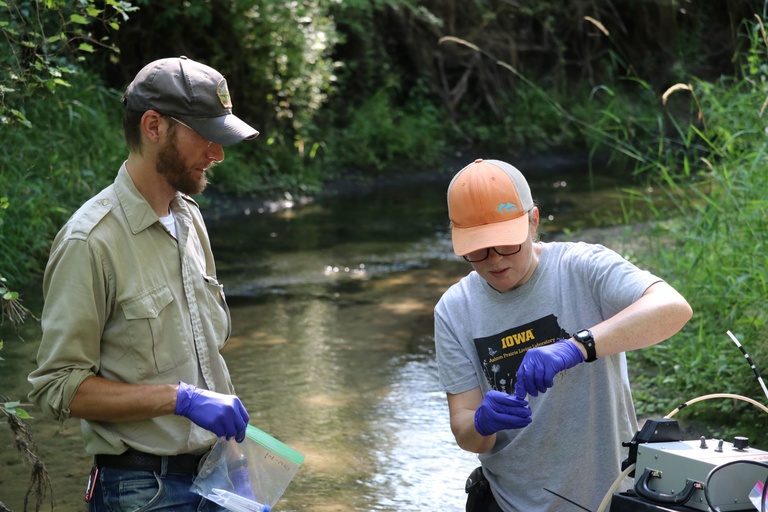 Two people collect samples from a creek