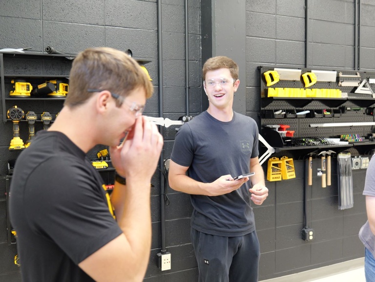 Two students wearing caps and safety goggles in a workshop.