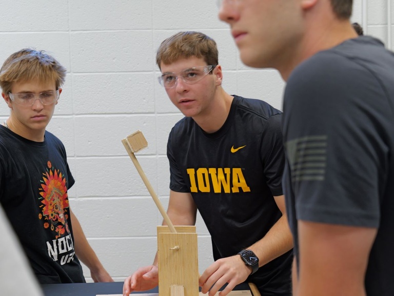 Students in a workshop environment, participating in a group project involving wooden components and tools.