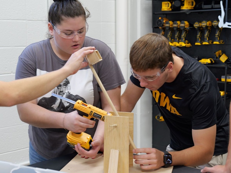 Students engaged in hands-on woodworking, focusing on assembling and aligning parts of a wooden structure.