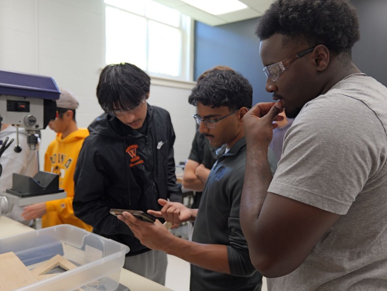 Students in a workshop environment, actively participating in a group project involving wooden components and tools.