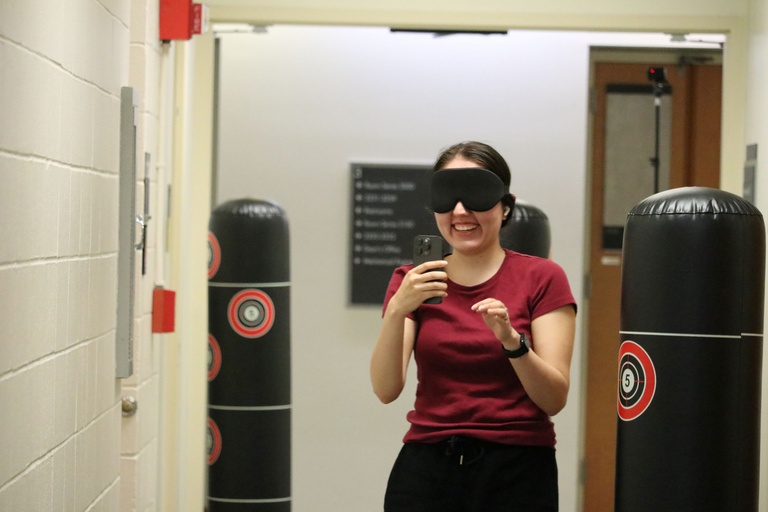 A person navigating a maze while wearing an eye mask and holding a cell phone