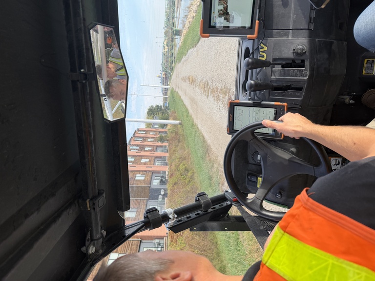 Man in orange safety vest drives UTV with apartments and river in background