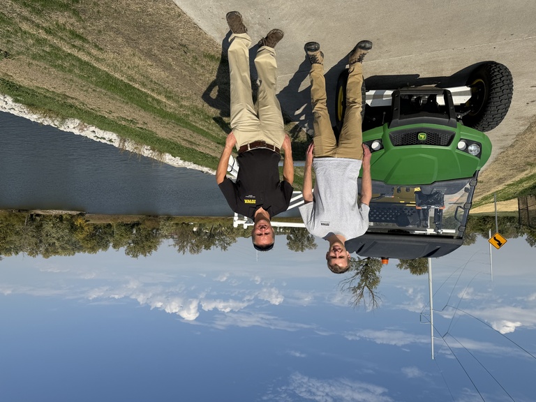 Two men pose in front of UTV a top levee and river in background