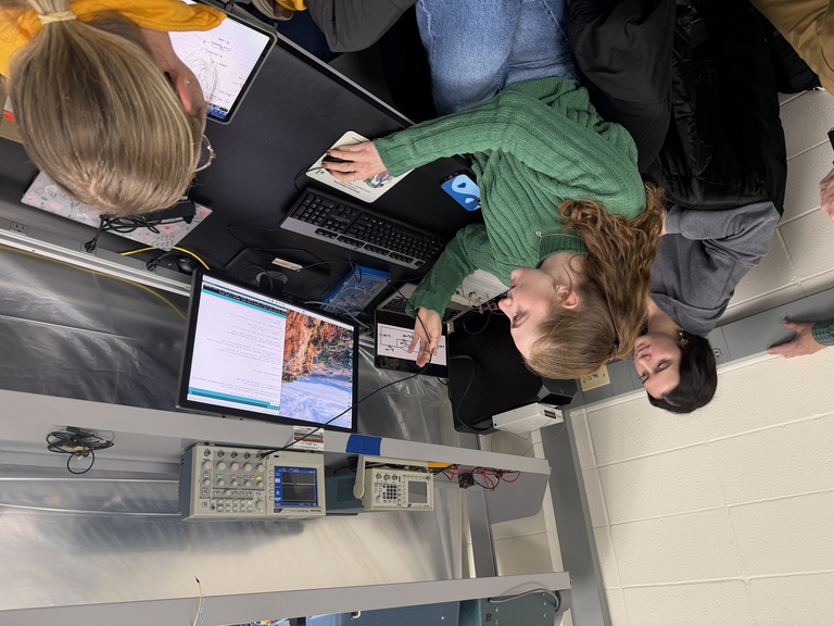 Woman in green shirt looks at computer monitor while two others look on