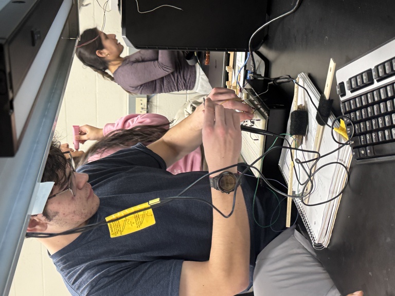 Man in navy shirt works on circuit at lab bench