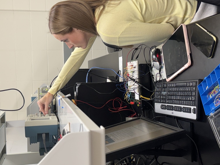 Seated woman in yellow shirt reaches to shelf 