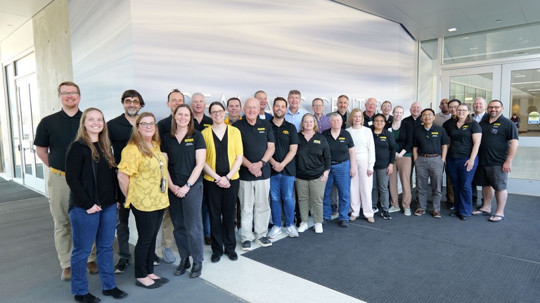 A large group of people stand together indoors for a group photo.