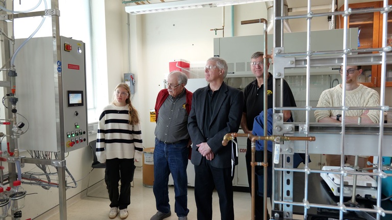 Visitors gathered in an engineering laboratory, standing near control panels, piping structures, and research equipment during a tour.