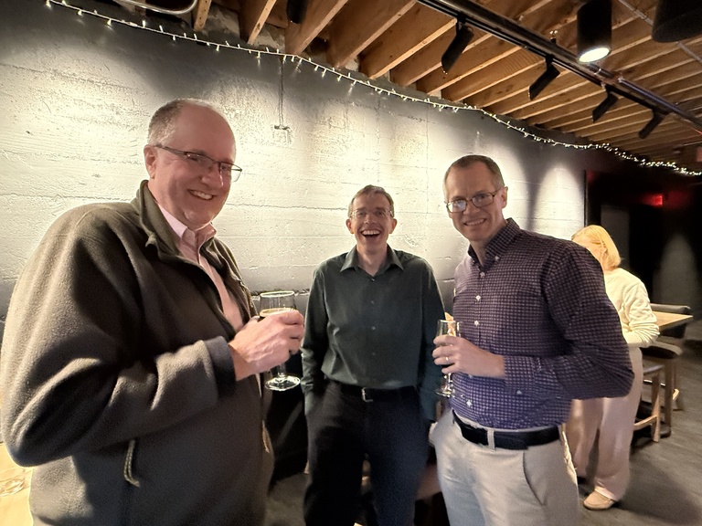 Three people standing together holding drinks in a casual indoor setting.