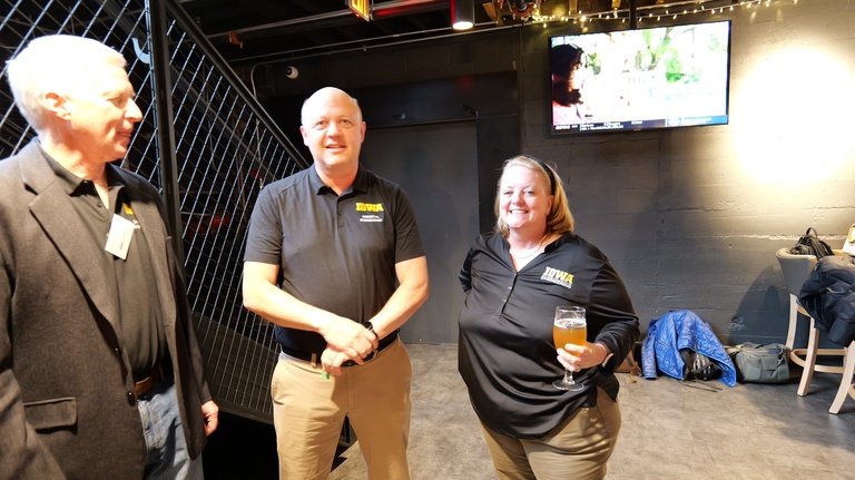Three people standing together holding drinks in a dimly lit gathering space.