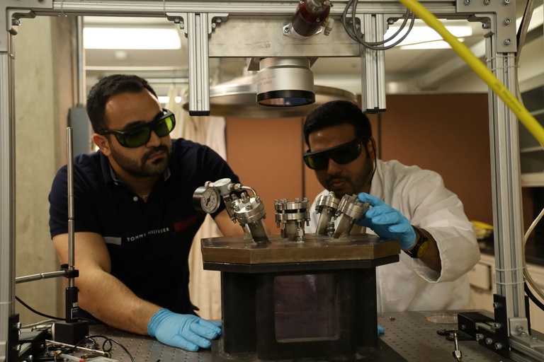 Two men look closely at a metal chamber on a lab bench.