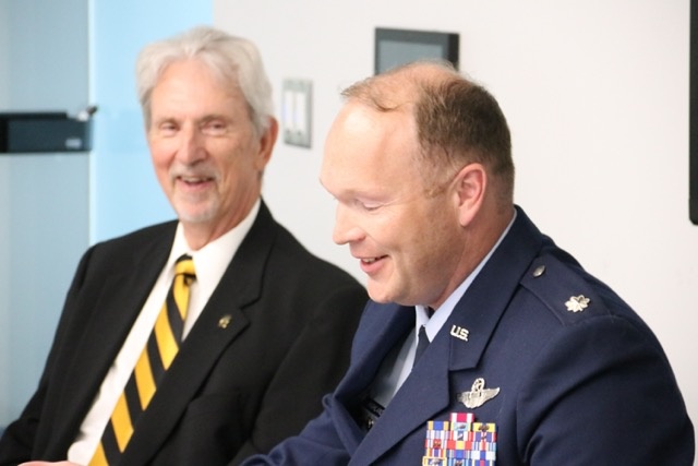 Man in military uniform (right) speaks with second man looking on
