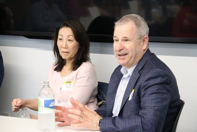Man in suit coat speaks while woman in white shirt looks on