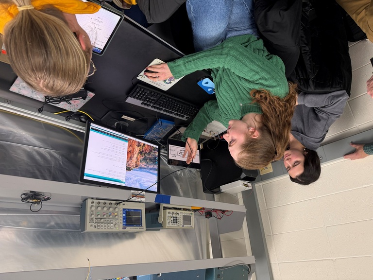 Woman in green shirt looks at computer monitor while two others look on