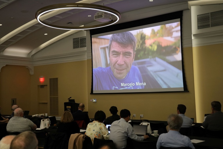 Projector screen displays man delivering virtual message during meeting