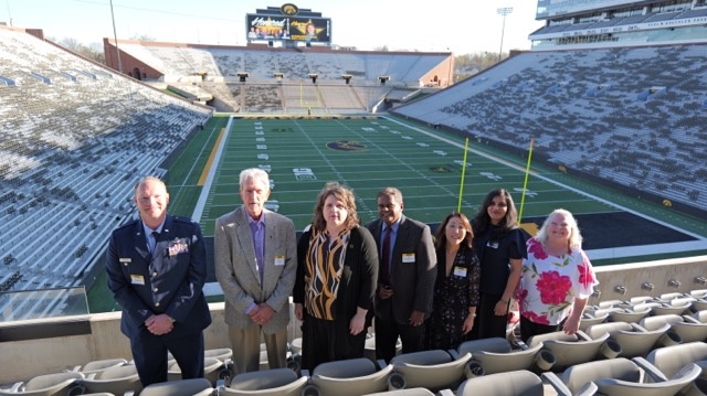 Seven people pose outside in stadium