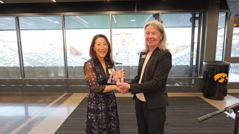 Woman in black dress coat (right) presents trophy to woman with dark hair