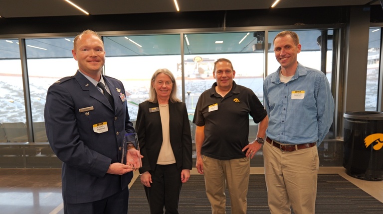 Man in military attire (right) poses with trophy with three others by his side