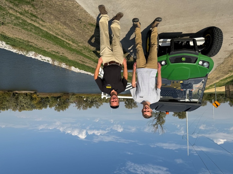 Two men pose in front of UTV a top levee and river in background