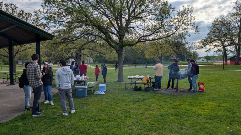 Group of students gathered at a park shelter and grill area during an outdoor cookout.